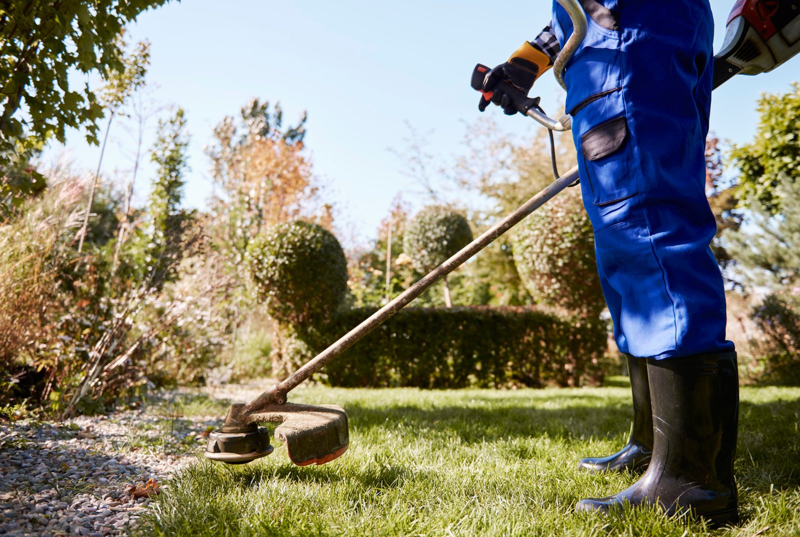 gardener-with-weedwacker-cutting-grass-garden-scaled.jpg